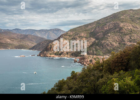 Ciel gris au-dessus d'une tour génoise sur un promontoire rocheux qui s'avance dans les eaux turquoises de la mer méditerranée à porto avec une vue le long de la côte ouest de la cor Banque D'Images