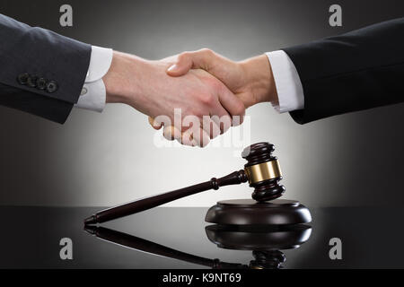 Close-up of two businessman shaking hands in front of mallet Banque D'Images