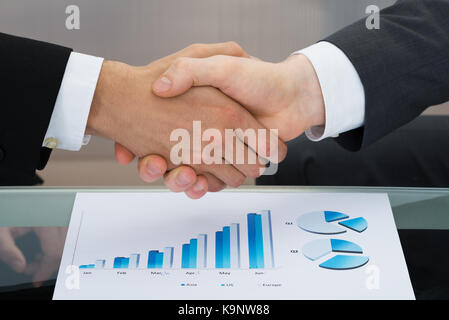 Close-up of two businessman shaking hand in front of graph Banque D'Images