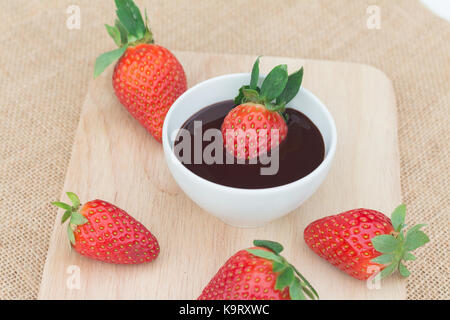 Fruits rouges fraises trempées dans le chocolat et servir sur plaque de bois. Banque D'Images
