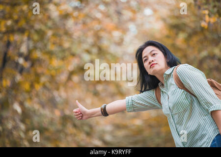 Asian woman backpacker debout sur route de campagne et l'auto-stop pour voiture avec arbre en automne automne,saison voyage seul ou seule concept voyageur Banque D'Images