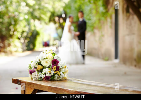 Bouquet sur banc en bois avec Bride and Groom à l'arrière-plan, l'accent sur les fleurs. Banque D'Images