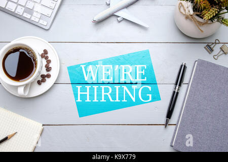 Nous recrutons, télévision lay concept de poste de travail. composition de tasse de café, carnet de notes, stylo, crayons, trombones toy airplane et tableau fleur sur wo Banque D'Images