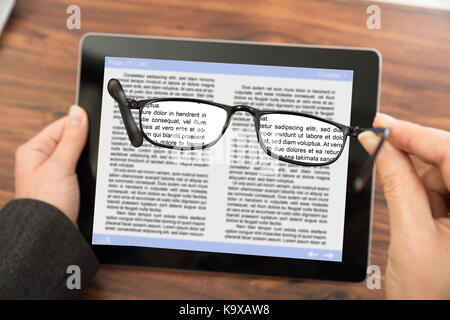 Personne de lecture d'e-livre sur la tablette numérique avec des lunettes Banque D'Images