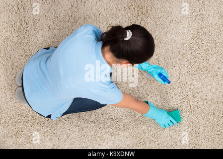 Jeune femme tapis de nettoyage avec un détergent vaporisateur et d'une éponge Banque D'Images