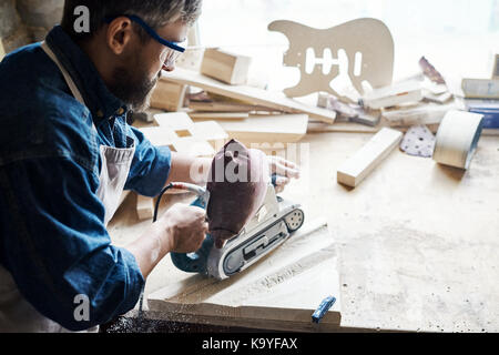 Vue arrière portrait d'artisan qualifié le ponçage pièce de bois dans la région de carpenters workshop fenêtre contre Banque D'Images