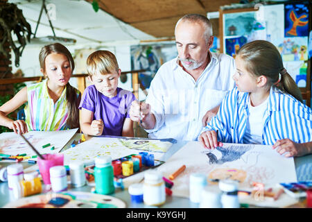 Portrait d'homme barbu enseignement groupe d'enfants peinture at desk in art studio Banque D'Images