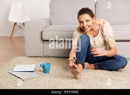 Belle femme heureuse à la maison faire une pause à la peinture ses ongles Banque D'Images