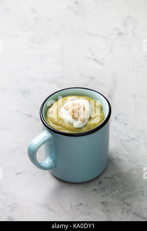 Soupe verte purée avec la crème, les noix de pin dans une tasse bleue sur un fond de béton gris. Banque D'Images