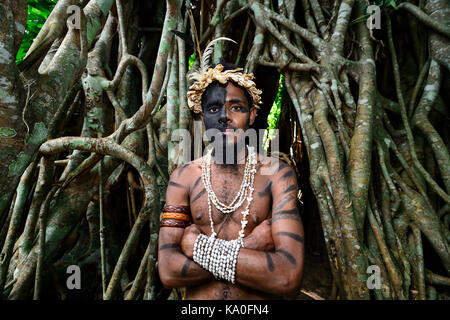 Guerrier Tribal devant les racines de l'arbre de banian (Ficus benghalensis), ekasup village culturel, l'île d'Efate, Vanuatu Banque D'Images