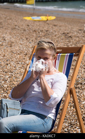 Femme assise dans un transat au bord de la mer, souffrant d'un écoulement nasal. s'être mouché le nez Banque D'Images