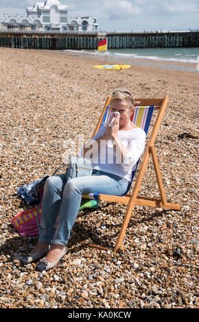 Femme assise dans un transat au bord de la mer, souffrant d'un écoulement nasal. s'être mouché le nez Banque D'Images