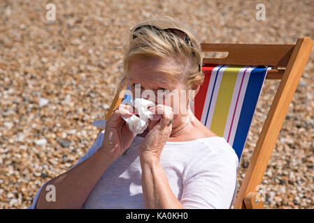Femme assise dans un transat au bord de la mer, souffrant d'un écoulement nasal. s'être mouché le nez Banque D'Images