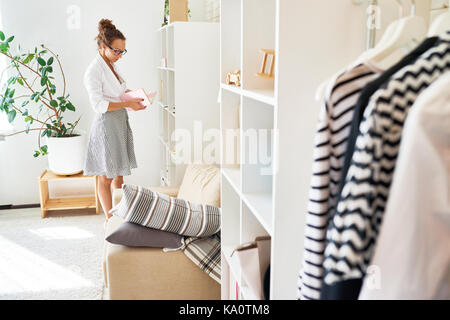 Portrait of young woman reading book élégant tout en se tenant par l'armoire dans appartement moderne Banque D'Images