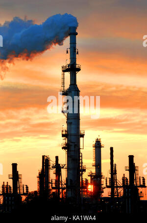 Les teintes d'orange le ciel du soir alors que le soleil se couche derrière la cheminée de la raffinerie de pétrole de rouleaux à vapeur. pile comme la vapeur est réglementé et libéré. Banque D'Images