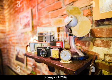 Le côté portrait de l'étagère en bois plein de vieilles lampes, horloges et vintage camera placée sur le mur de brique décorée de tableaux. Banque D'Images
