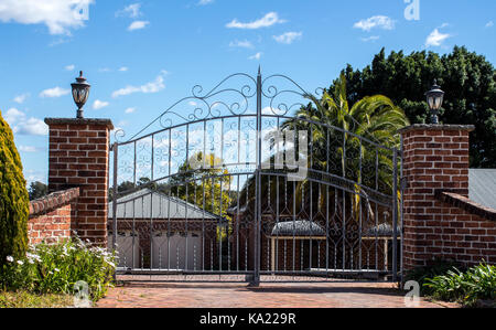 L'entrée des portes d'entrée de sécurité en métal situé dans quartier résidentiel avec jardin clôture en brique en arrière-plan contre le ciel bleu Banque D'Images