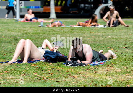 Couple relaxing, bronzage et lecture des comprimés sur l'herbe sur l'Esplanade, Cairns, Far North Queensland, Queensland, Australie, FNQ Banque D'Images