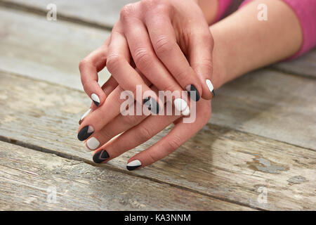 Femme élégante avec mains manucure. manucure noir et blanc créatif sur les mains, le vieux fond de bois. Banque D'Images