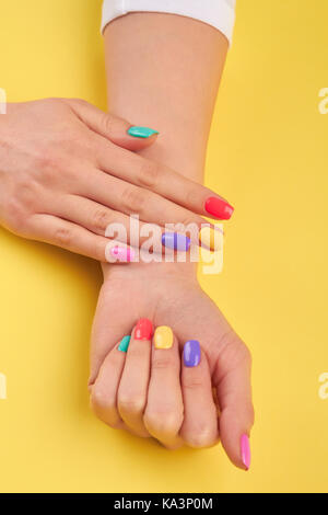 Les mains de womans avec couleurs d'ongles manucure femme multicolore. jaune sur fond d'été. Banque D'Images