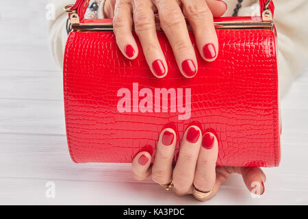 Sac à main rouge élégant de femmes. femme âgée avec mains manucure rouge laqué holding close up. sac à main moderne de womans accessoire. Banque D'Images