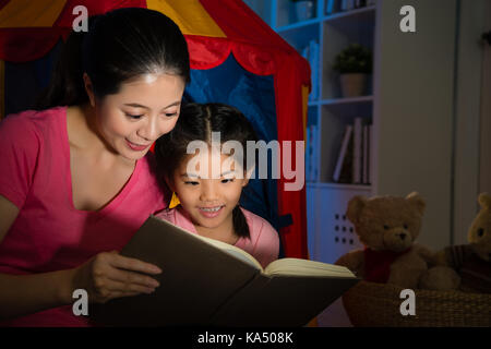 Belle petite fille douce histoire lecture bande dessinée la nuit sur chambre avec bonheur maman élégantes bénéficiant d'coucher assis en face de toy 10 Banque D'Images