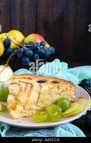 Un grand morceau d'une Tarte aux poires et raisins sur une plaque sur un fond de bois sombre. Banque D'Images