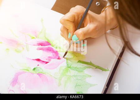 Close-up artist avec clous lumineux attire une fine brosse en bois et d'aquarelle dans l'album pour l'élaboration de pivoines rose avec des feuilles vertes Banque D'Images