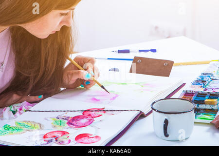 Artiste brune avec des clous lumineux attire une fine brosse en bois et d'aquarelle dans l'album pour dessiner sur du papier blanc de pivoines rose, sur le tableau w Banque D'Images