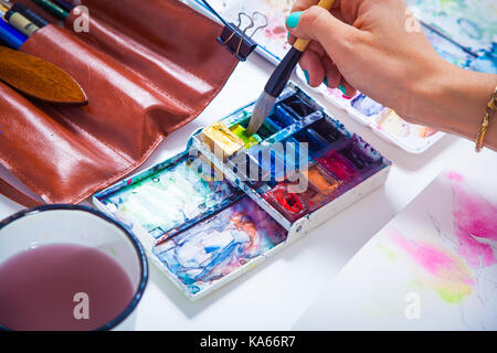 Une femme dessine un portrait d'une femme avec une brosse en bois et à l'aquarelle dans une feuille de travail, sur la table se trouvent un étui en cuir avec des brosses, un dessin, sac Banque D'Images