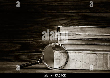 Photo en noir et blanc. une pile de vieux livres et la loupe sur fond de bois. Le concept de la recherche, l'étude de l'espace pour le texte. Banque D'Images