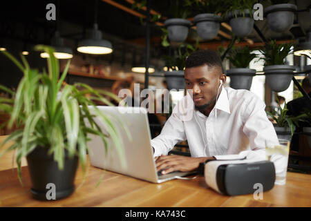 African man typing at laptop, reposant dans le café. Banque D'Images