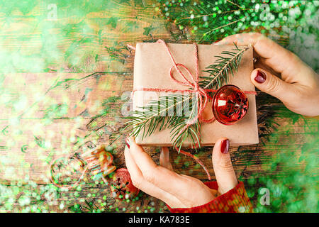 Woman's hands donner enveloppé de Noël ou d'autres vacances boîte cadeau fait main en papier avec un ruban rouge. présent fort, décoration sur table en bois, vue du dessus wi Banque D'Images