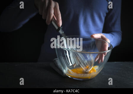Battre les jaunes dans un bol en verre avec un fouet sur fond violet l'horizontale Banque D'Images