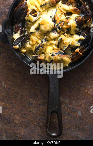 Poêle avec moules sous de la sauce au fromage sur un fond brun à la verticale Banque D'Images