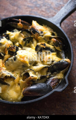 Poêle avec moules sous une sauce au fromage sur un fond brun vertical diagonal Banque D'Images