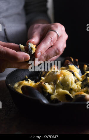 Les mains sur une poêle avec la sauce au fromage moules sous la verticale Banque D'Images