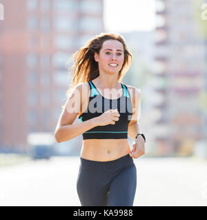 Young smiling sporty woman running on road rue du matin. fitness girl jogging en ville Banque D'Images