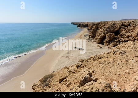 Plage de sable avec une falaise spectaculaire et un ciel bleu clair à Ras Al Jinz, Oman, offrant amplement d'espace pour des arrière-plans à thème de voyage et des concepts de destination Banque D'Images