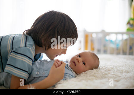 Beau garçon, serrant avec tendresse et soins son frère nouveau-né à la maison. famille amour bonheur concept Banque D'Images