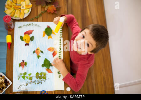 Mon petit enfant, garçon, l'application quitte en utilisant la colle alors que faire de l'artisanat à l'école, temps d'automne Banque D'Images