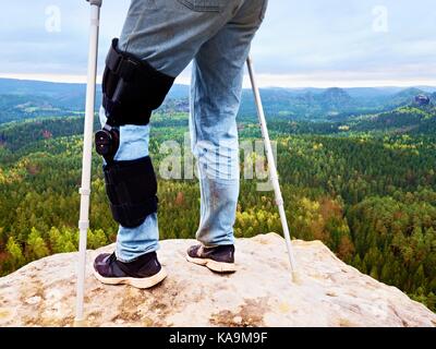 Close up de l'homme marchant avec des béquilles dans la nature. l'homme aux jambes en jeans avec bandage ajustable sur la douleur au genou. Banque D'Images