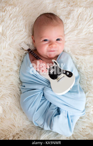 Bébé nouveau-né garçon, enveloppé dans l'écharpe bleue, tenant un peu de guitare et smiling Banque D'Images