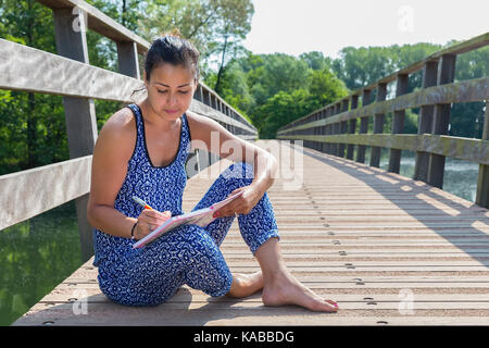 Jeune auteur féminin assis sur le pont de bois dans la nature Banque D'Images