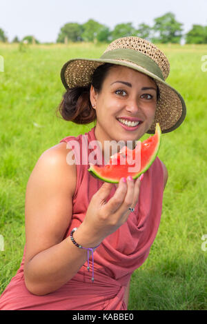 Young woman wearing straw hat eating fresh melon rouge dans la nature Banque D'Images