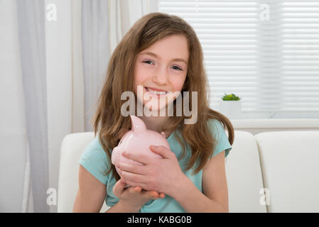 Portrait of cute girl holding pink piggy bank in hands Banque D'Images