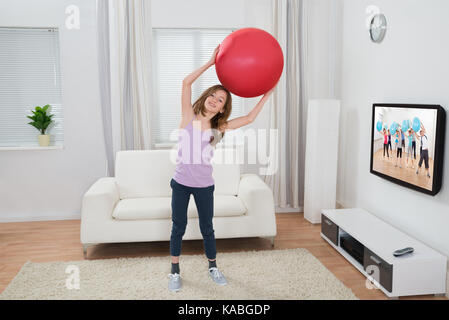 Happy girl holding fitness ball en face de la télévision à la maison Banque D'Images