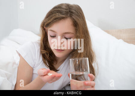 Fille sur le lit en tenant comprimé avec un verre d'eau dans la chambre Banque D'Images