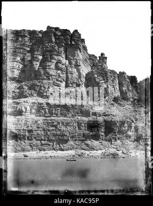 Cette photographie capture un petit bateau traversant le fleuve Colorado à Marble Canyon, dans le Grand Canyon, entre 1900 et 1930. L'image met en évidence les premières méthodes de transport utilisées dans le canyon et le terrain accidenté entourant la rivière. Banque D'Images