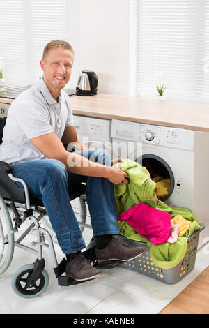 Jeune homme heureux sur fauteuil roulant enfiler ses vêtements dans la machine à laver Banque D'Images